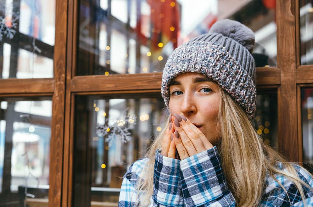 Young beautiful blonde girl blows and rubs her hands in the cold winter weather.