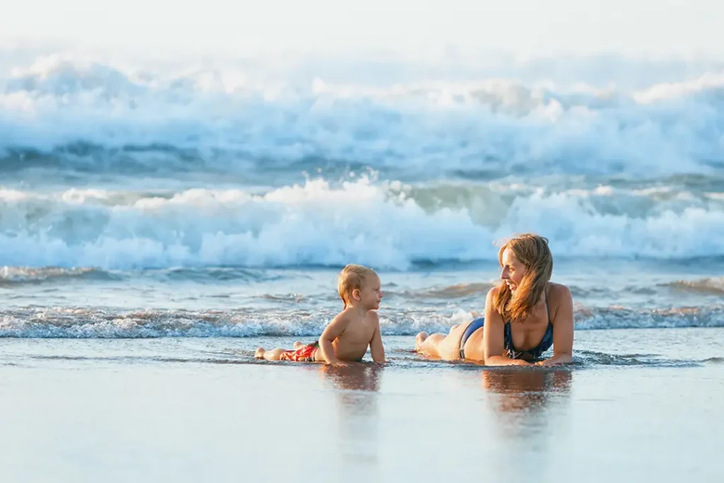 Smiling woman lying on the beach next to her child.