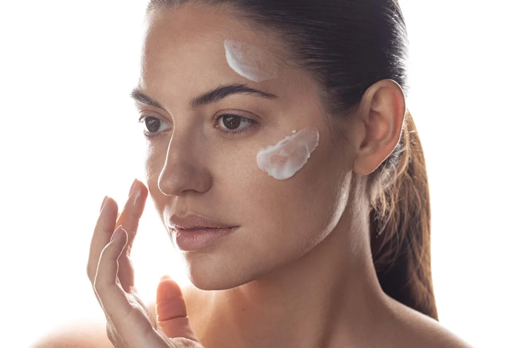 Beautiful young woman applying skin care product to her face